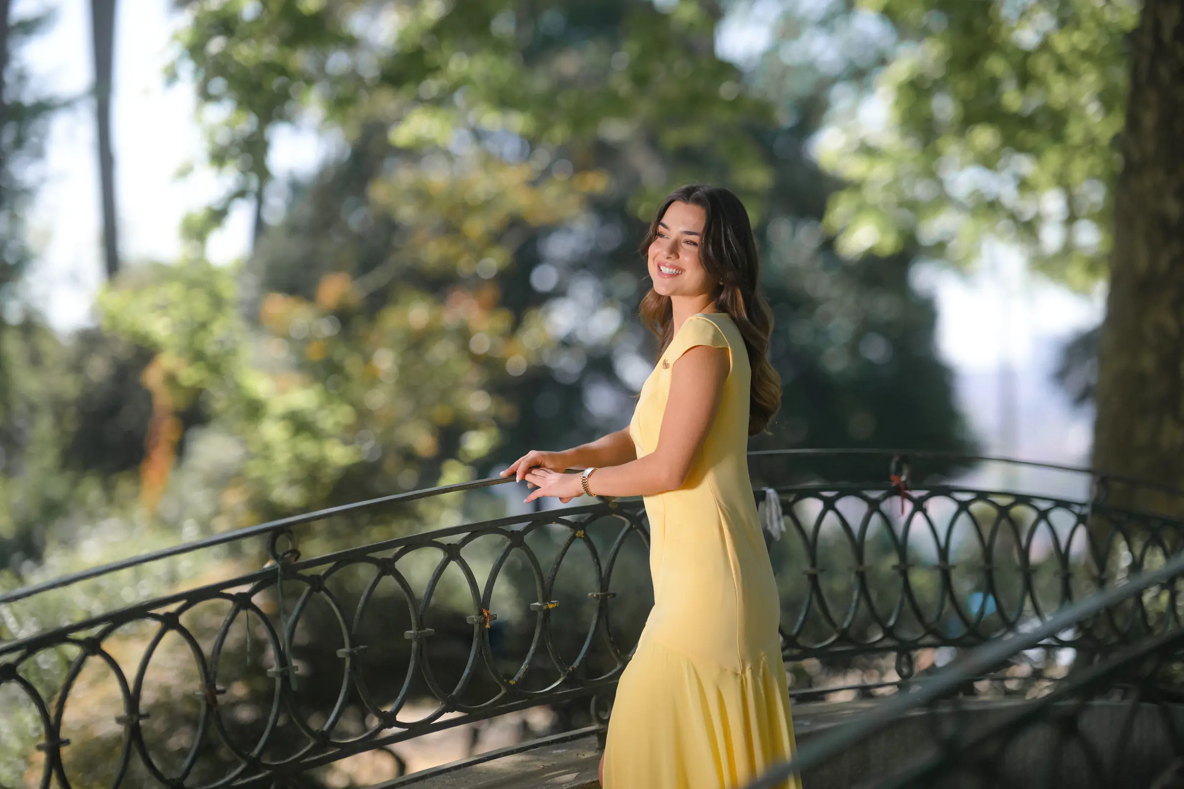 A woman in the yellow Copper Soul dress, leaning on a wrought-iron railing in a garden